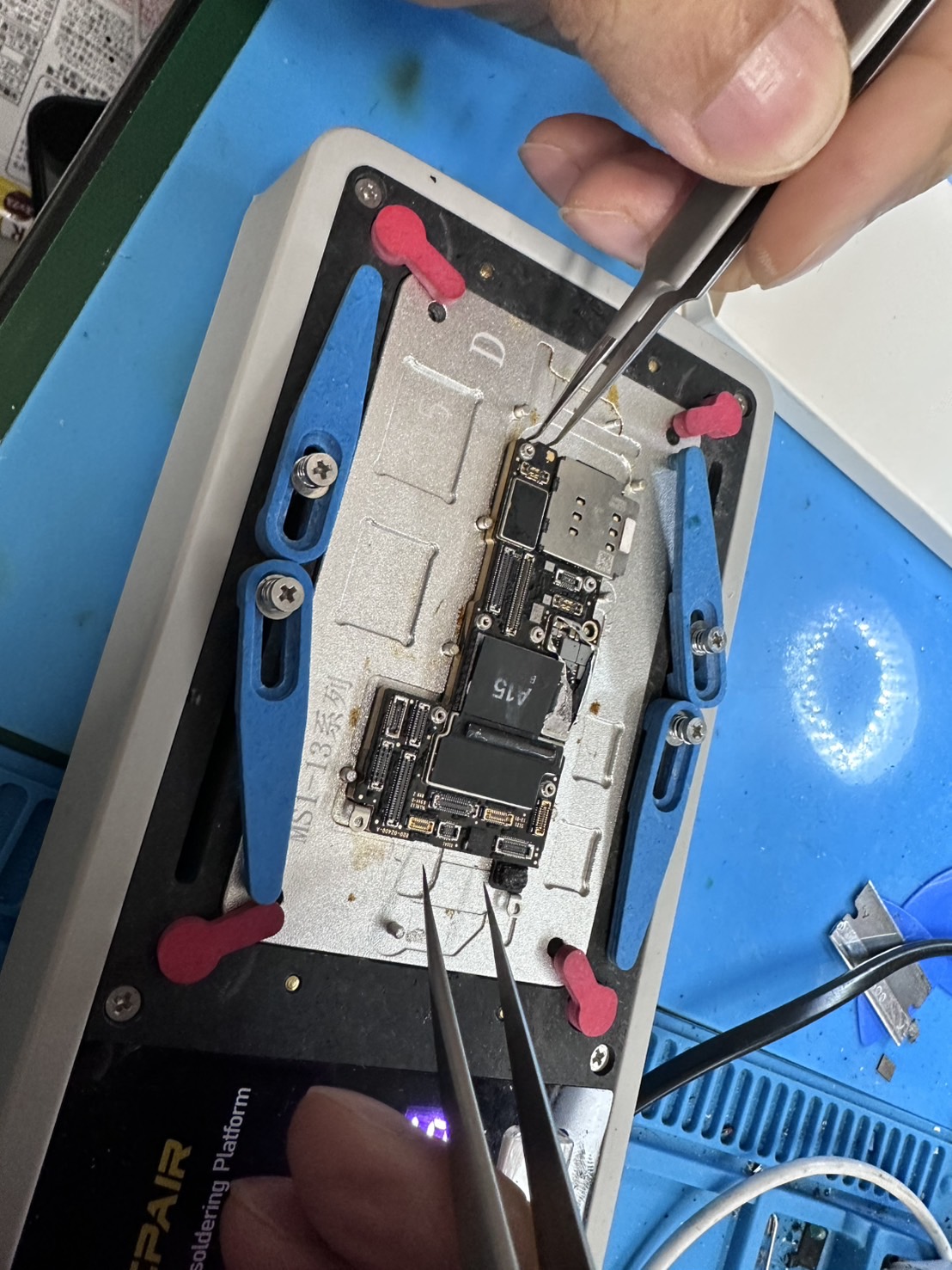 固定したスマートフォンの基板を、ピンセットで細かく作業している手元。